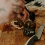 a person putting olives on a piece of bread